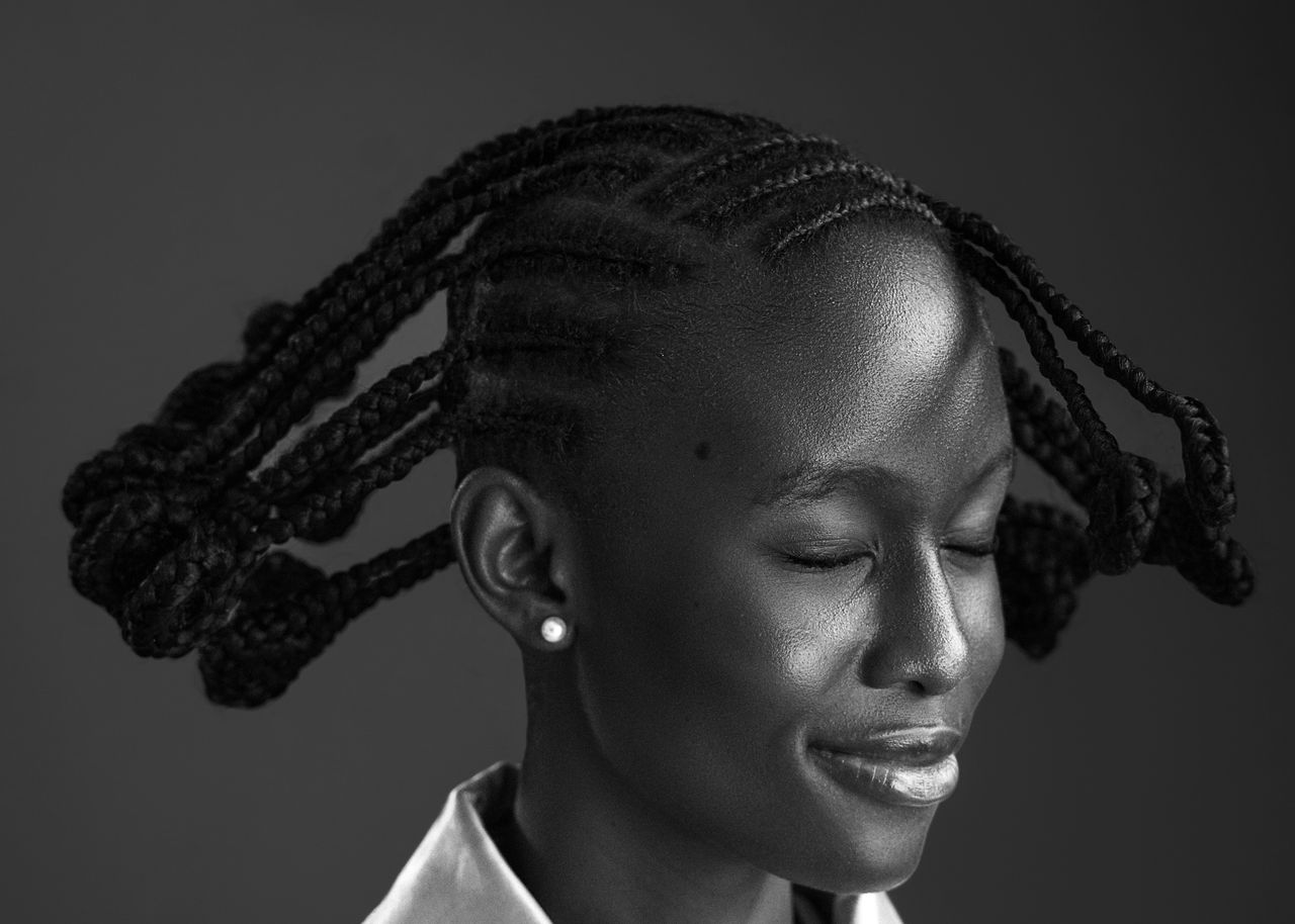 Black and white portrait of a smiling woman with braided hair and closed eyes.